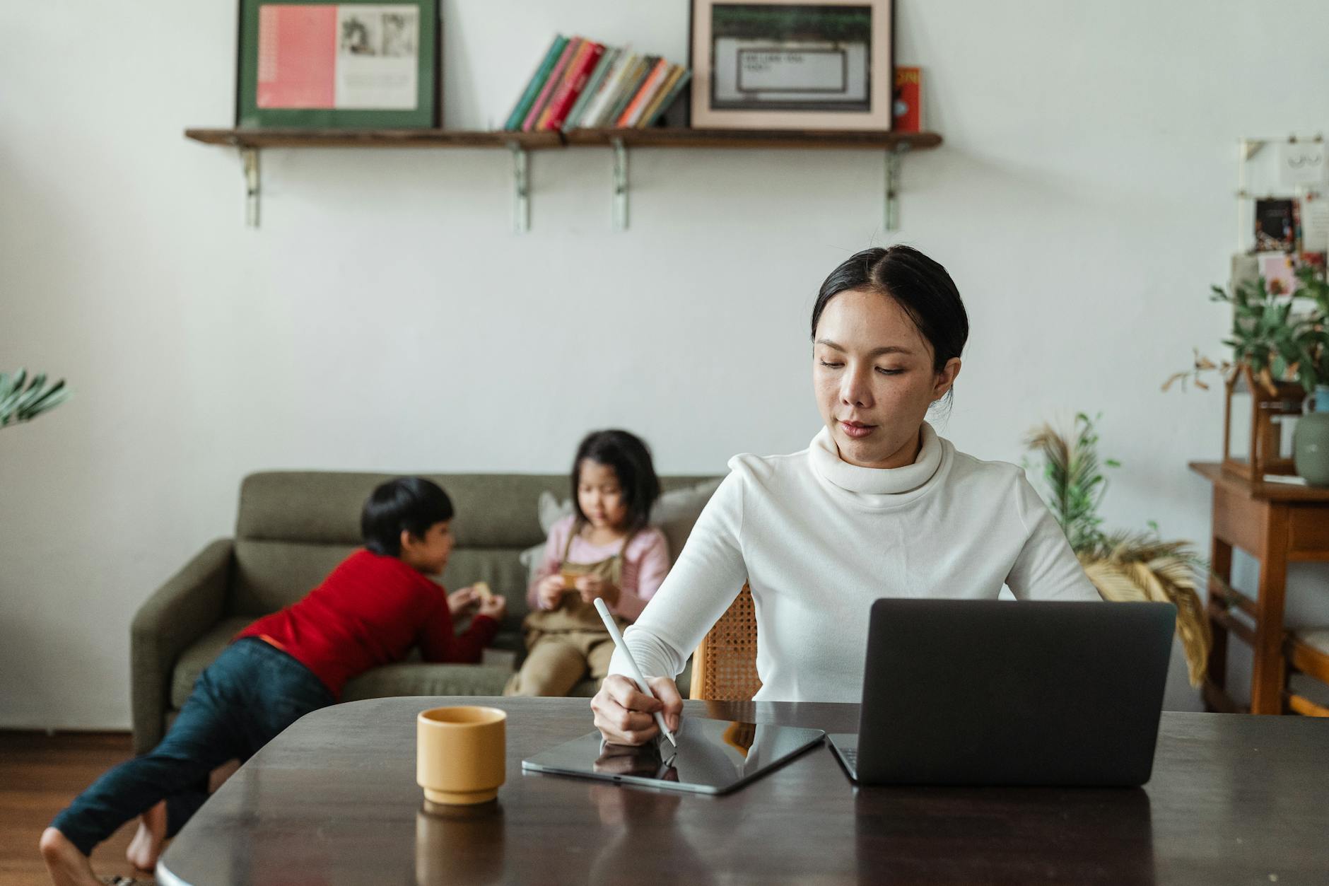 focused young mother working on custody arrangements while children playing on sofa